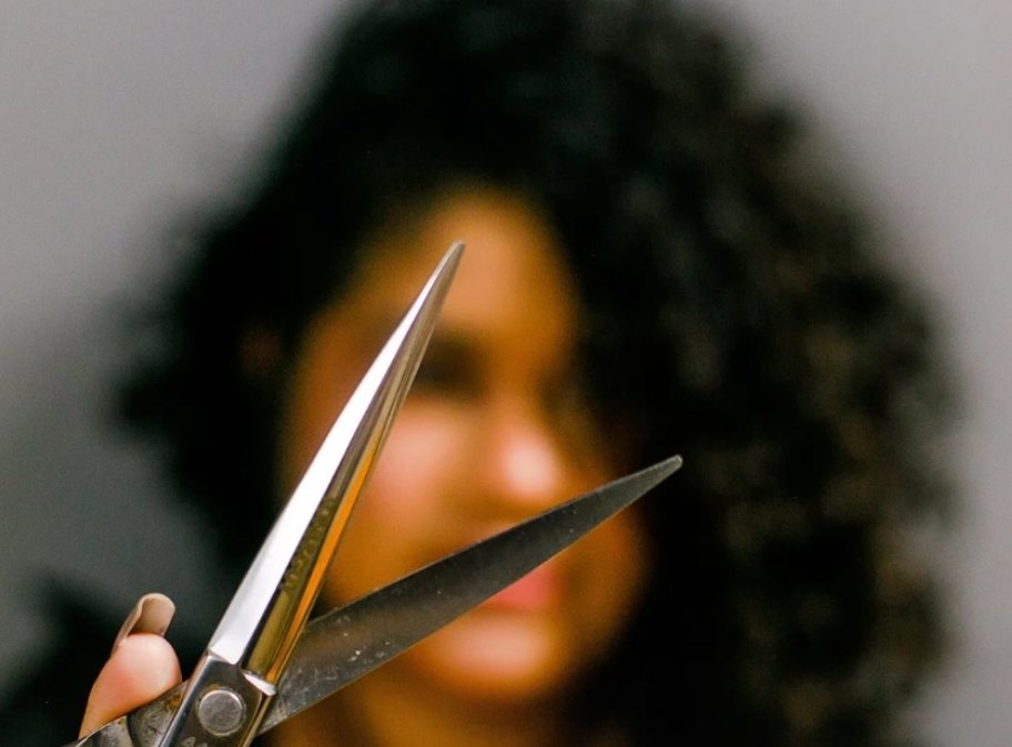 Profissional segurando tesoura de corte diante de uma cliente de cabelo cacheado